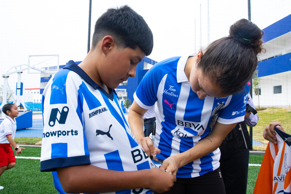 Jugadora del Club de Futbol Monterrey firmando una playera a uno de los niños beneficiados con la cancha