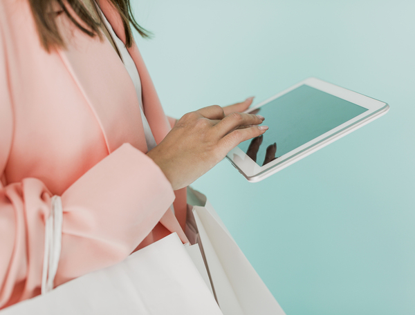 Mujer comprando en una tablet mientras sostiene bolsas de compras