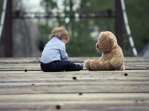 Bebé sentado junto a un oso de peluche 