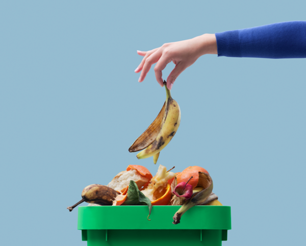 Una mano femenina depositando residuos orgánicos en un bote verde de reciclaje