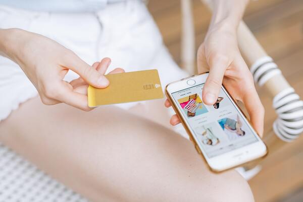Mujer comprando a través de su teléfono móvil mientras sostiene su tarjeta de crédito en la otra mano