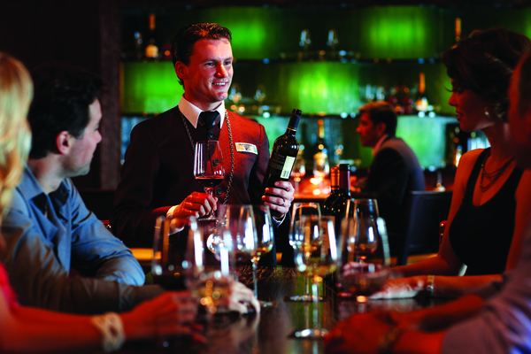 Sommelier atentiendo una mesa de 4 personas, con una cantina de fondo dentro en un crucero Celebrity