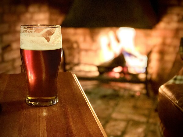 un vaso de cerveza oscura sobre una mesa frente a una chimenea