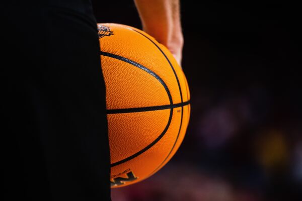 Foto de una persona vestida con uniforme negro de basketball y un balón de la NBA en la mano