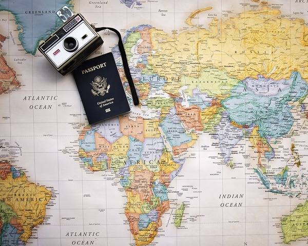 Foto de un mapa mundi, una cámara reflex y un pasaporte sobre lo que parece ser una mesa