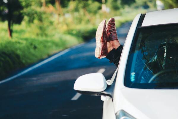 Auto en una carretera con un par de pies femeninos saliendo por la ventana