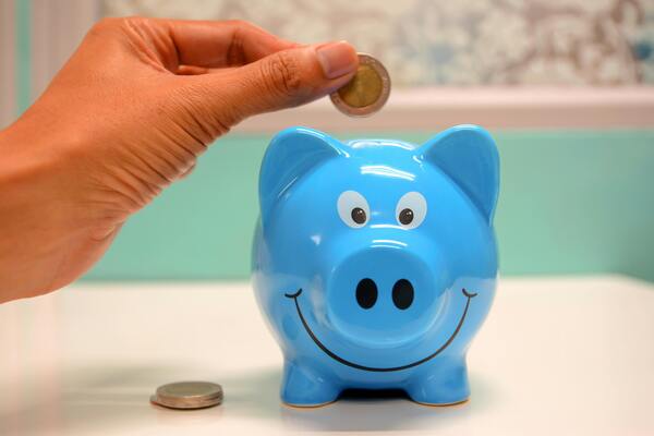 Mano masculina depositando una moneda en una alcancia de cerdo