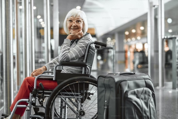 Mujer de la tercera edad sentada en su silla de ruedas esperando en una sala del aeropuerto mientras sonríe