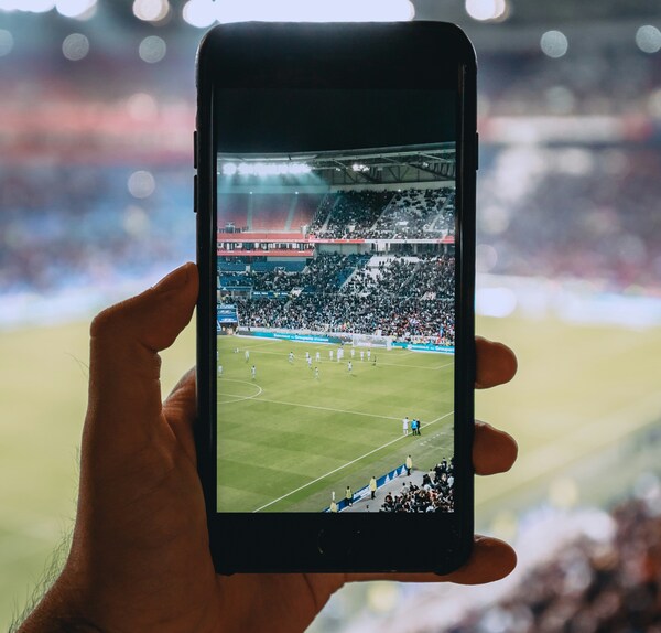 Mano masculina sosteniendo un smartphone para grabar un partido de soccer